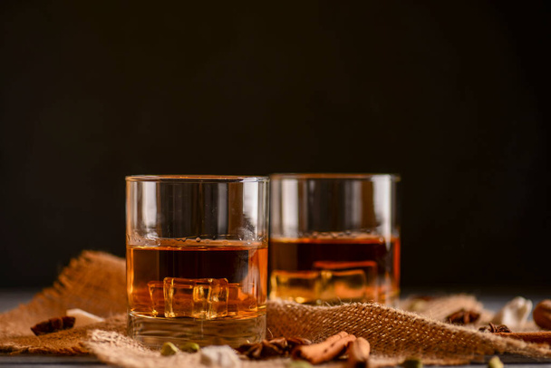 Scotch on wooden background with copyspace. Whiskey in shot glasses. Black background. Whiskey with cinammon and other spices. - Photo, image
