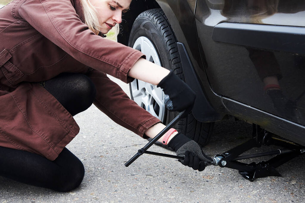 Uma jovem loira levanta o carro perto de seu carro com um pneu furado, problemas na estrada. - Foto, Imagem