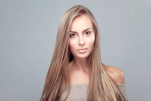 Portret van een meisje met perfecte huid en make-up, lang haar, blote schouders kijkend naar de camera, over grijze achtergrond. - Foto, afbeelding
