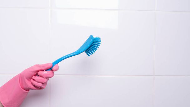 een vrouwelijke hand in een handschoen houdt een wasborstel vast - Foto, afbeelding