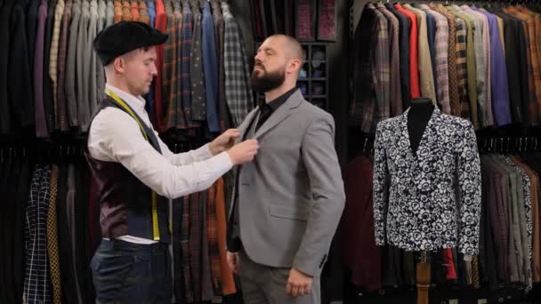 男性のテーラードデザイナーは、服店で男性モデルの測定テープでスーツを測定します。ブティックコンセプト - 映像、動画