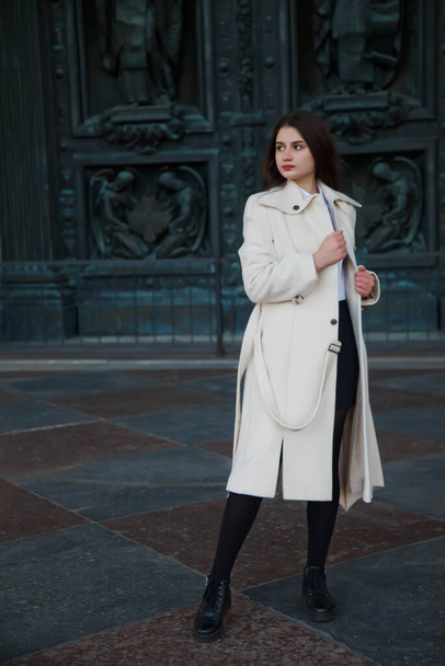 Fashionable young beautiful stylish woman in white coat walking on street. Autumn fashion trend for smiling, happy, purposeful female. Concept style, fashion, beauty and achievement goals. Copy space - Foto, Imagen