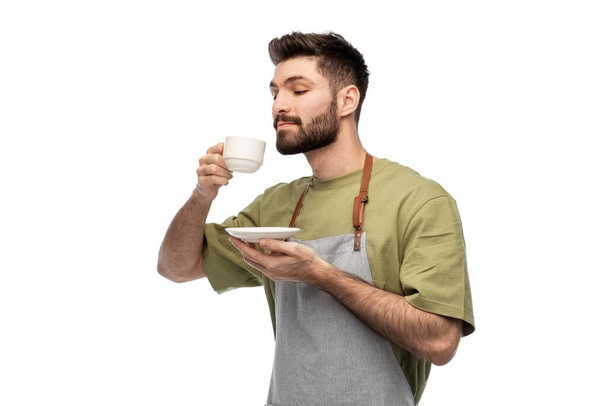 happy barista or waiter in apron drinking coffee - Foto, afbeelding