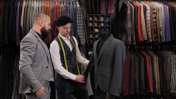 Slow motion of handsome man choosing a suit design with tailor in atelier. designer presenting the costume on the menequin to the buyer at the clothing store - Footage, Video