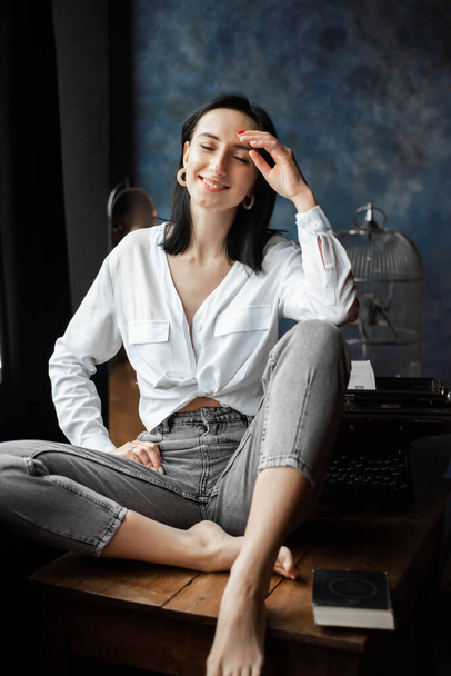 Woman at home sitting on a table wearing white shirt - Foto, afbeelding