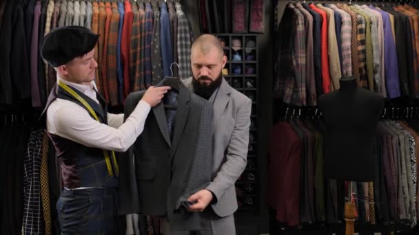 Slow motion van knappe man die een kostuumontwerp kiest met kleermaker in atelier. ontwerper presenteert de Blazer aan de koper in de kledingwinkel - Video