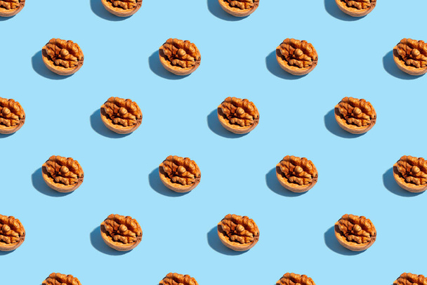Seamless regular pattern with walnuts on a light blue background. Hard light. The concept of vegetarianism and proper nutrition. - Photo, image