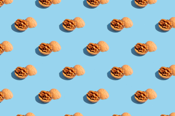 Seamless regular pattern with walnuts on a light blue background. Hard light. The concept of vegetarianism and proper nutrition. - Foto, immagini