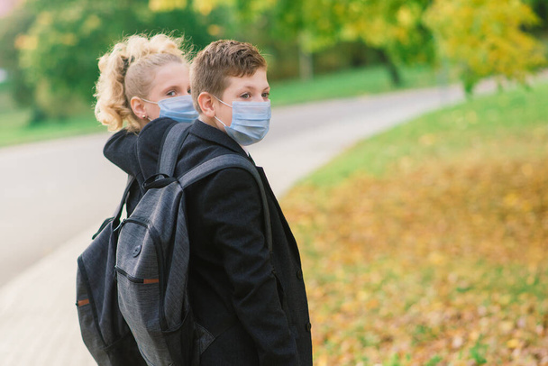 scolari, ragazzo e ragazza in maschere mediche a piedi nel parco della città. - Foto, immagini