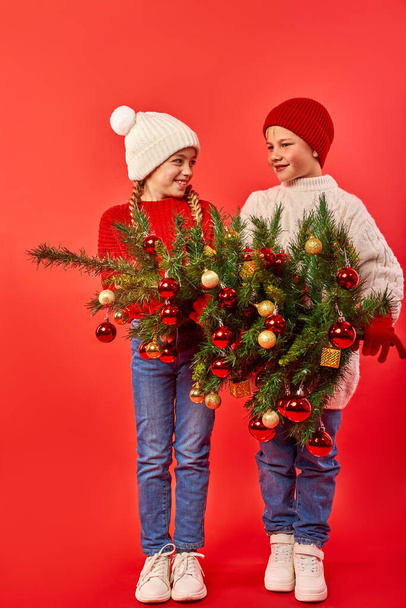 studio portrait of happy kids with a small Christmas tree on red isolated background - Fotoğraf, Görsel