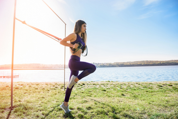A sportos nő a szabadban edz a TRX-szel nappal. Teljes test ellenállás gyakorlatok neki egészséges életmód. - Fotó, kép