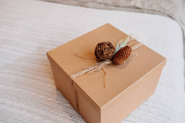 cuadrado Corton eco-friendly caja de regalo decorada con cono de pino y ramita de abeto en la cama acogedora, embalaje reutilizable, enfoque selectivo - Foto, imagen