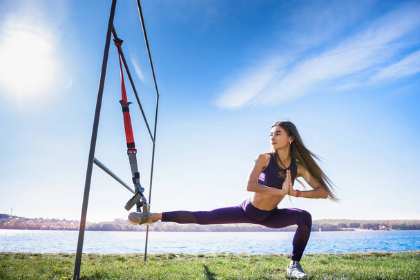 jonge vrouwelijke atleet die 's ochtends traint met trx fitnessbanden in het park. Concept van gezonde training en levensstijl - Foto, afbeelding
