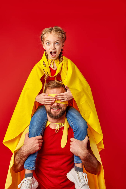 shocked girl sits on neck of father closing his eyes, superhero - Φωτογραφία, εικόνα