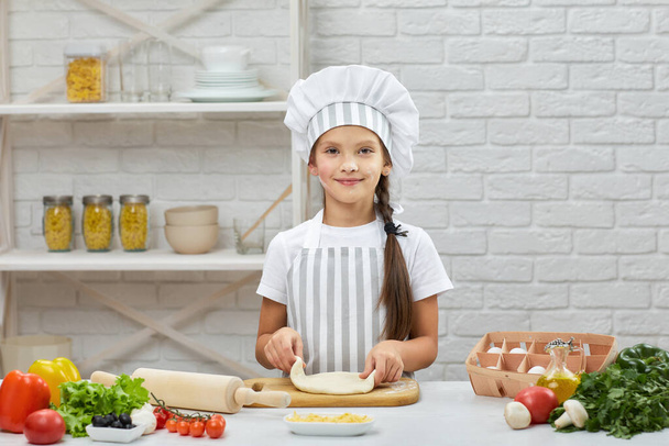 little child girl in cap and an apron knead the dough - Fotoğraf, Görsel