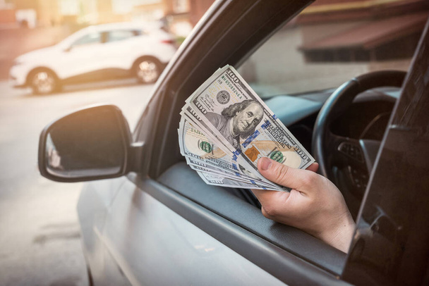 businessman pays for a product or service, gives dollars while sitting in the car. finance concept - Photo, Image