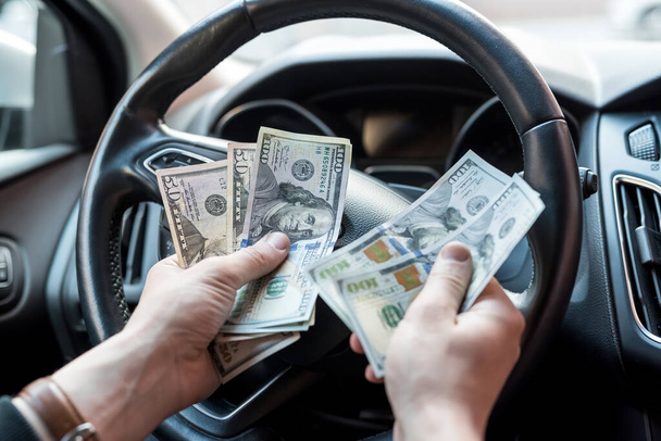 Hombre sentado en un coche contando billetes de dólar para o como sobornos, seguros o crédito, invirtiendo. venta o alquiler de automóviles - Foto, imagen