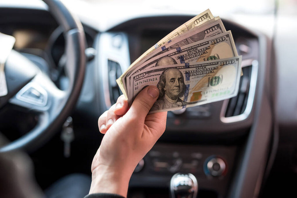 Hombre sosteniendo dólares sentado en el coche. comprar o alquilar, sobornar - Foto, imagen