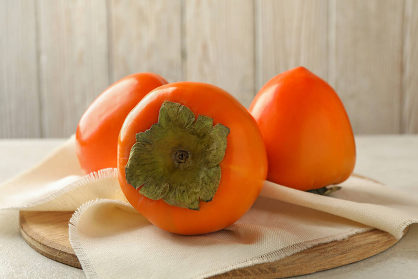 Board with persimmon on white table, close up - Foto, imagen