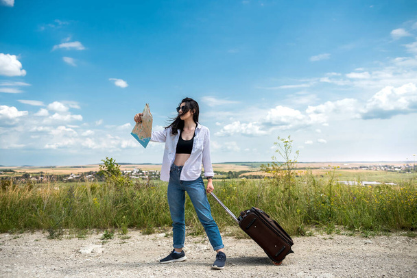 turista femenina con un mapa caminando por una carretera en un día soleado de verano. concepto de vacaciones - Foto, Imagen