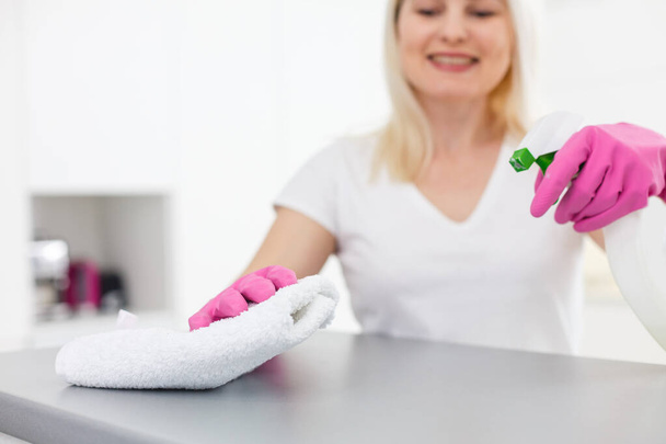 台所の女性は彼女の家を掃除しながら、スプレーとダスターを使用してほこりを笑って拭く、クローズアップ - 写真・画像