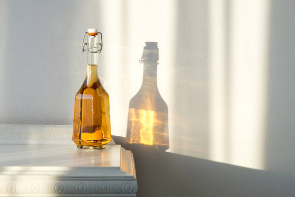 Elegante bottiglia con alcol e vetro vuoto su un mobile vintage e un bellissimo riflesso di sole sulla parete - concetto di arte - Foto, immagini