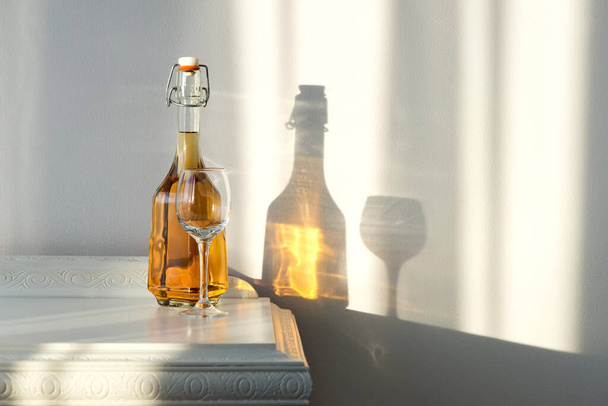 Elegantní láhev s alkoholem a prázdným sklem na vinobraní skříňky a krásným slunečním odrazem na stěně - umělecký koncept - Fotografie, Obrázek