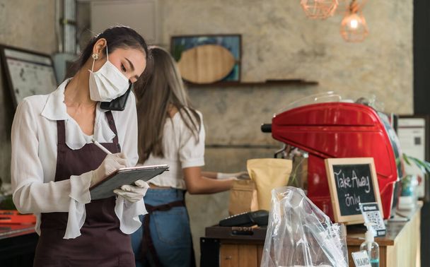 Asian waitress take order from mobile phone for takeout and curbside pickup orders while city lockdown. They wear protective face mask to prevent from infection of coronavirus COVID-19 pandemic. - Photo, Image