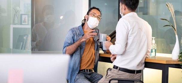 Panoramic Two office workers talking while coffee break in new normal with social distance practice office.  They wear face mask reduce risk to infection of COVID-19 coronavirus as new normal life. - Фото, изображение