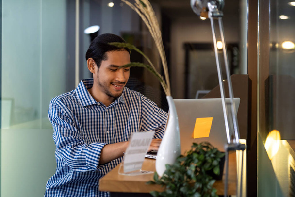 Young adult Asian businessman sitting at coffee bar in office with laptop. Smart office work everywhere concept. - Foto, afbeelding