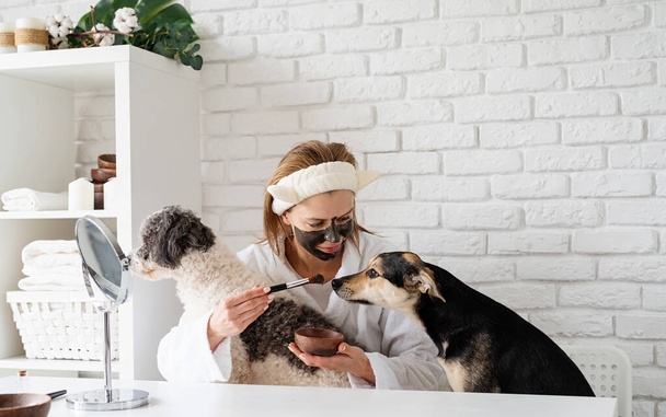 Young caucasian woman wearing bathrobes doing spa procedures with her dog - Foto, Imagen