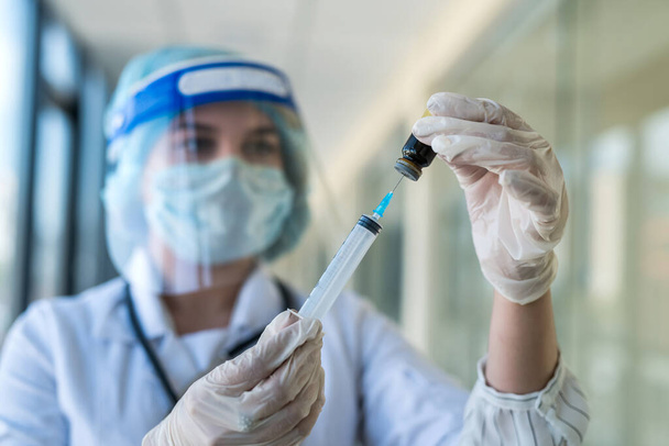 bonita enfermera con uniforme y protector facial sosteniendo la jeringa y esperando vacunación en la clínica - Foto, imagen