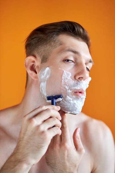 caucasian man with white foam on his face, isolated on orange background - Fotoğraf, Görsel
