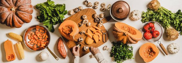 Fall, winter vegan cooking ingredients layout. Flat-lay of female hands cutting mushrooms over white plain table with pumpkins, celery, corn, sweet potato, top view. Vegan, vegetarian, clean eating - Zdjęcie, obraz