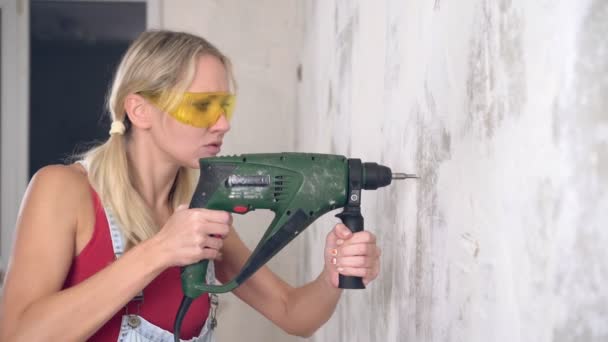 Een jonge vrouw boort een muur met een elektrische hamer of boor - Video