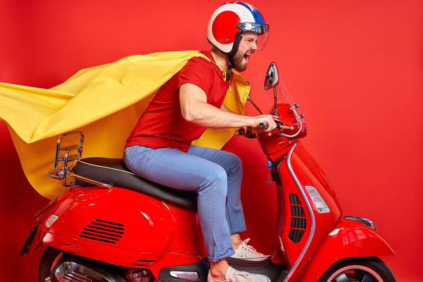 crazy guy drive moped wearing cloak and helmet rushing road party in super heroes role - Foto, immagini