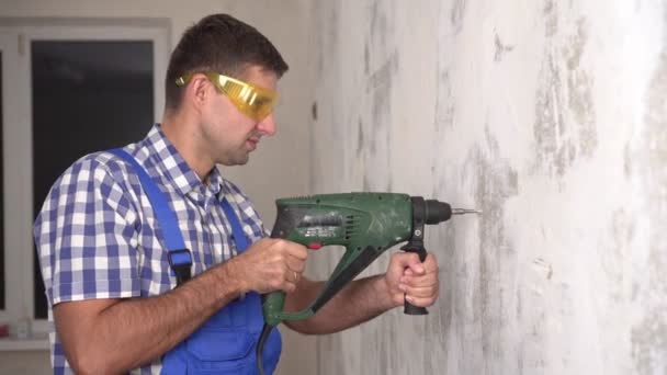Un operaio maschio trapana un muro con un martello elettrico e mostra i pollici in alto - Filmati, video