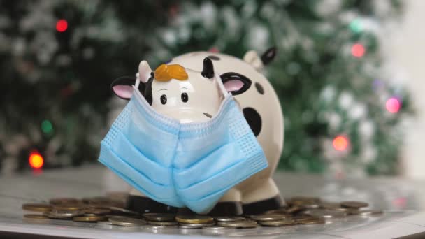 Piggy τράπεζα ειδώλιο με τη μορφή αγελάδας ή ταύρου σε ιατρική μάσκα. Ο αντίκτυπος της πανδημίας στην οικονομία. Χέρια με ένα κουμπαρά από κοντά - Πλάνα, βίντεο
