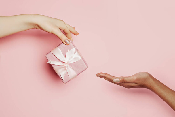 Woman hand giving pink gift taking hand on pink, minimal background composition - Foto, Imagem