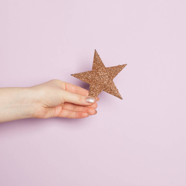 Minimal Christmas background card. Beautiful female hand holding golden Star on lilac background - 写真・画像