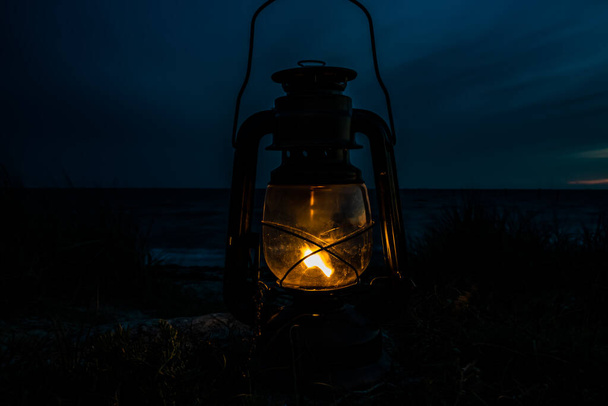 Antigua linterna de aceite clásica que arde con una llama naranja junto al océano al atardecer. .. Foto de alta calidad - Foto, imagen