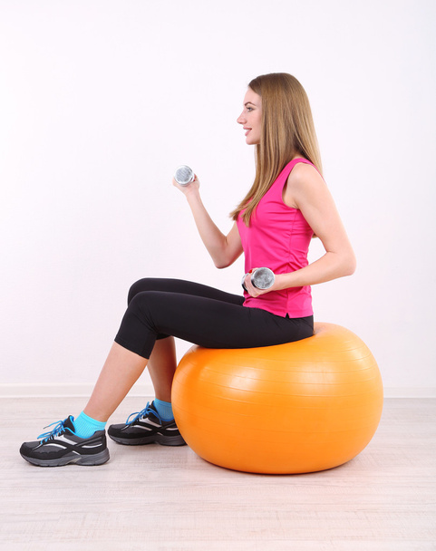 Young beautiful fitness girl exercising with orange ball and dumbbells in gym - Fotografie, Obrázek