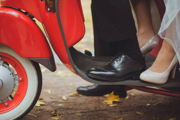 Une photo recadrée unique de marié et mariée chevauchant sur la moto rouge à l'automne. Chaussures de mariée et marié sur le scooter. Jour de mariage inoubliable avec équitation extrême - Photo, image