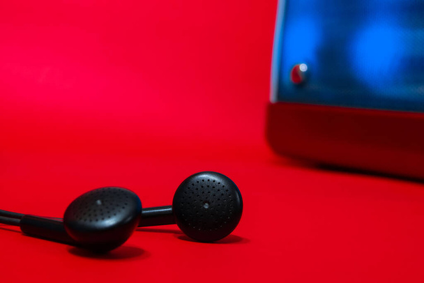 certains écouteurs noirs bien focalisés sur l'un d'eux avec un haut-parleur avec rétroéclairage hors foyer et tout le fond rouge - Photo, image