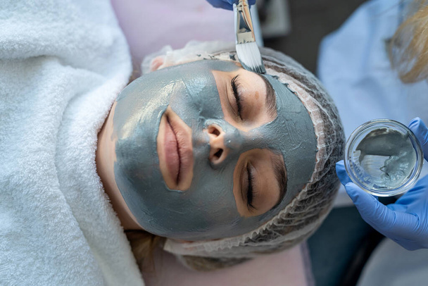 Kosmetologe macht dunkle Maske auf Gesicht junge hübsche Frau in Spa Salon. Professionelle Hautpflege. - Foto, Bild