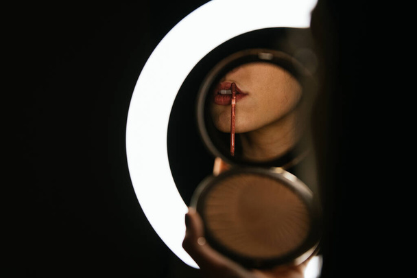 model painting her lips through a lighted mirror - Foto, Bild