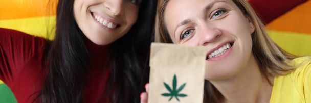 Two women are holding a lgbt flag and paper bag with marijuana sign - Photo, Image