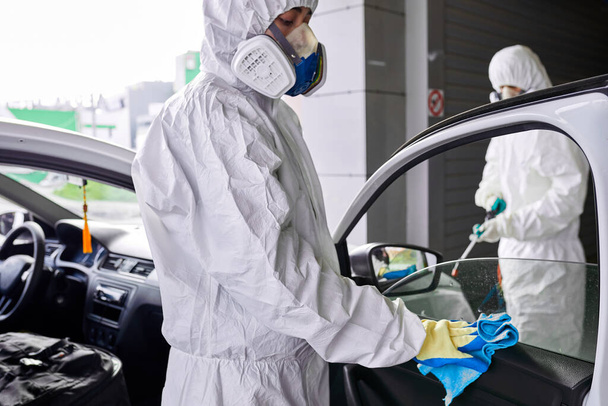команда санитаров в защитном костюме для чистки автомобиля - Фото, изображение