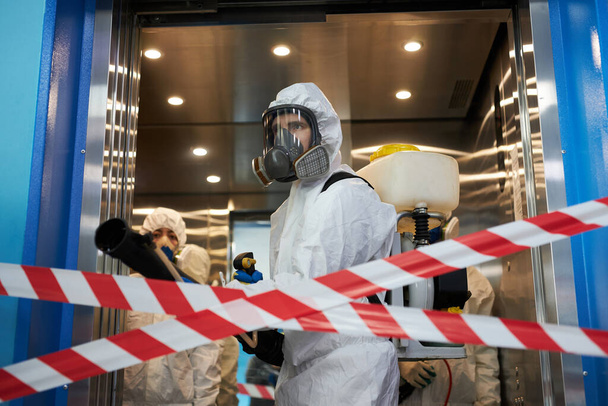 workers in hazmat suits and face mask protection while making disinfection indoors - Фото, изображение