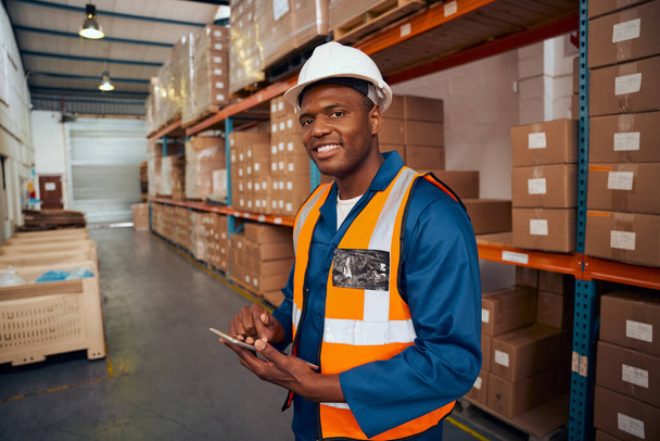 Smiling portrait of a african warehouse worker holding digital tablet in hand looking at camera - Fotó, kép